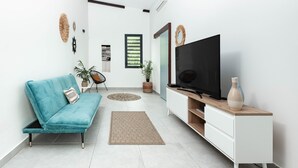 A modern living room with a teal sofa, a flat-screen TV on a wooden stand, a white cabinet, and decorative wall art.