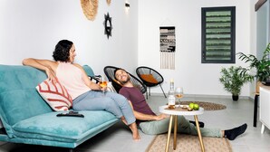 A living room with a teal sofa, a round coffee table, and a small side table with a bottle and a glass.
