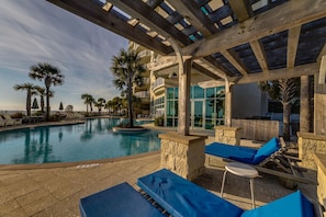 A pool area with lounge chairs, a pergola, and a view of the ocean. - Aqua Resort 1111 (Panama City Beach)