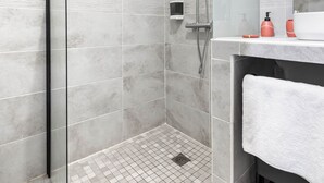Een moderne badkamer met een douche, een glazen deur, een betegelde vloer en een wastafel met een handdoek.