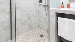 Un bany modern amb un envàs de dutxa de vidre, una tovallola blanca i un mirall sobre el lavabo.
