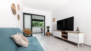 Un saló modern amb un sofà blau, una televisió sobre un moble blanc i vista a l'exterior a través d'una finestra gran.