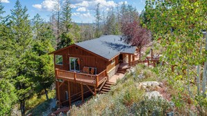 A wooden cabin with a balcony, surrounded by trees and a mountainous backdrop.