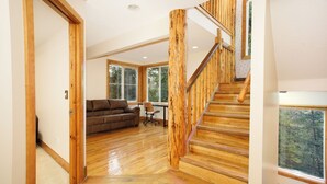 A spacious living area with a wooden staircase, large windows, and a cozy sofa.