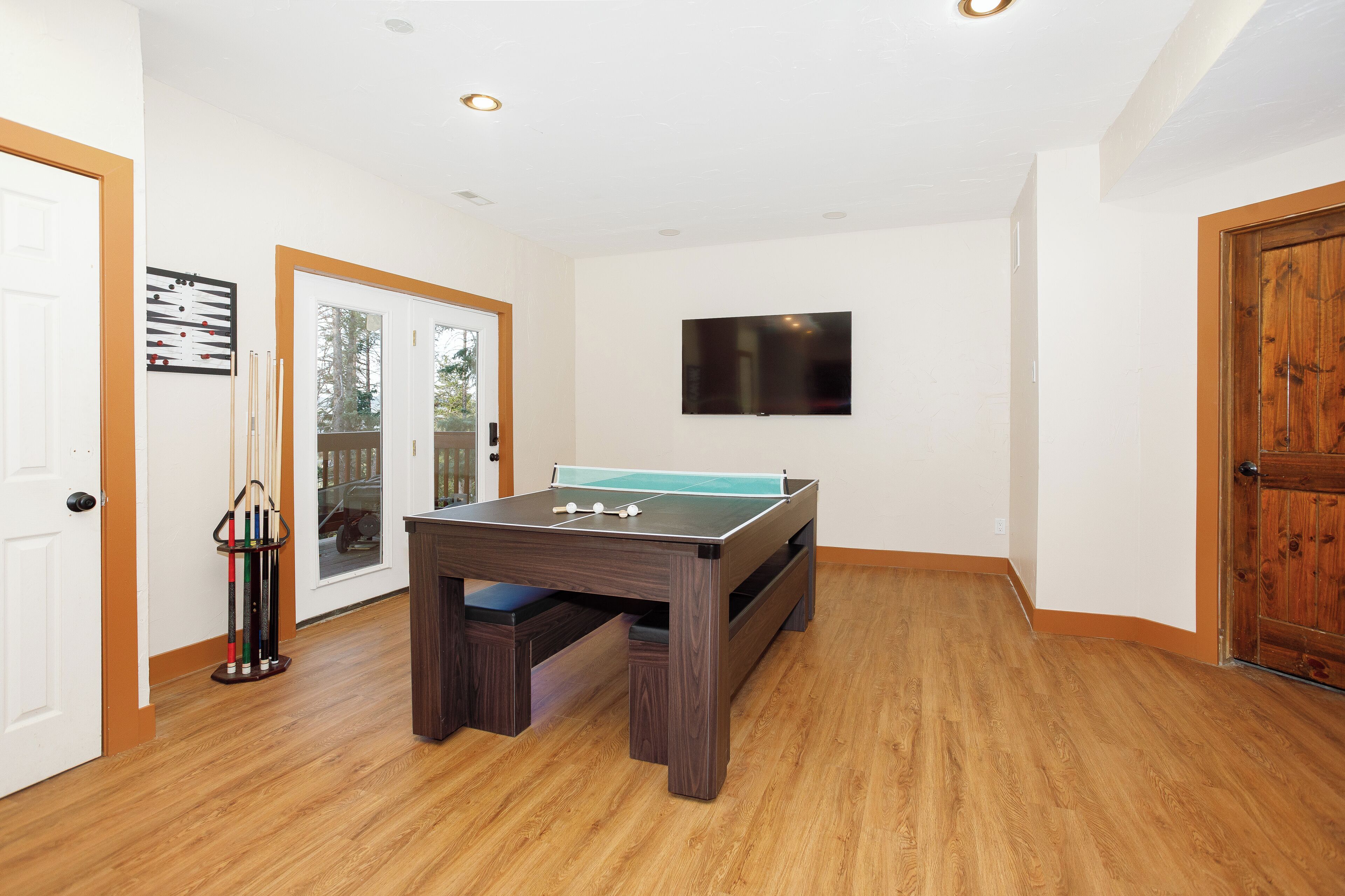 Una habitación con mesa de fútbol, televisor montado en la pared y una puerta con panel de vidrio.
