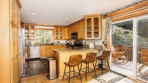 A kitchen with wooden cabinets, a central island with bar stools, a dishwasher, and a view of a deck with outdoor furniture.