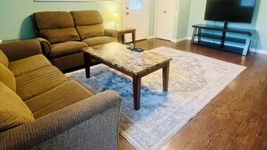 A living room with a brown sofa, a coffee table, a TV, and a window with blinds. - Charming Cozy Cabin in a PEACFUL MOUNTAIN setting w HOTTUB! Close to PigeonForge (Seymour)
