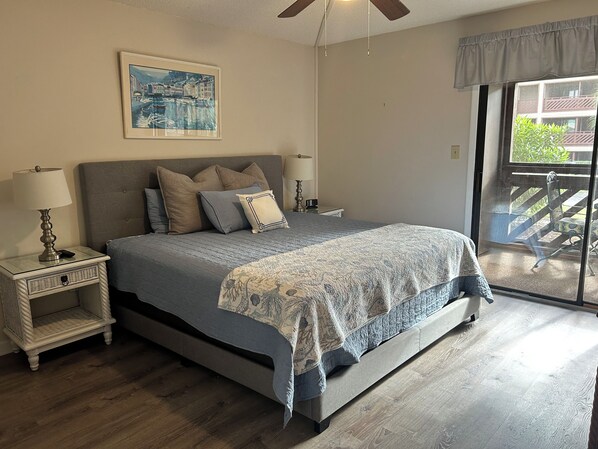 Une chambre à coucher avec un lit, des tables de chevet, un ventilateur de plafond, une fenêtre donnant sur un beau paysage et un tableau accroché au mur.