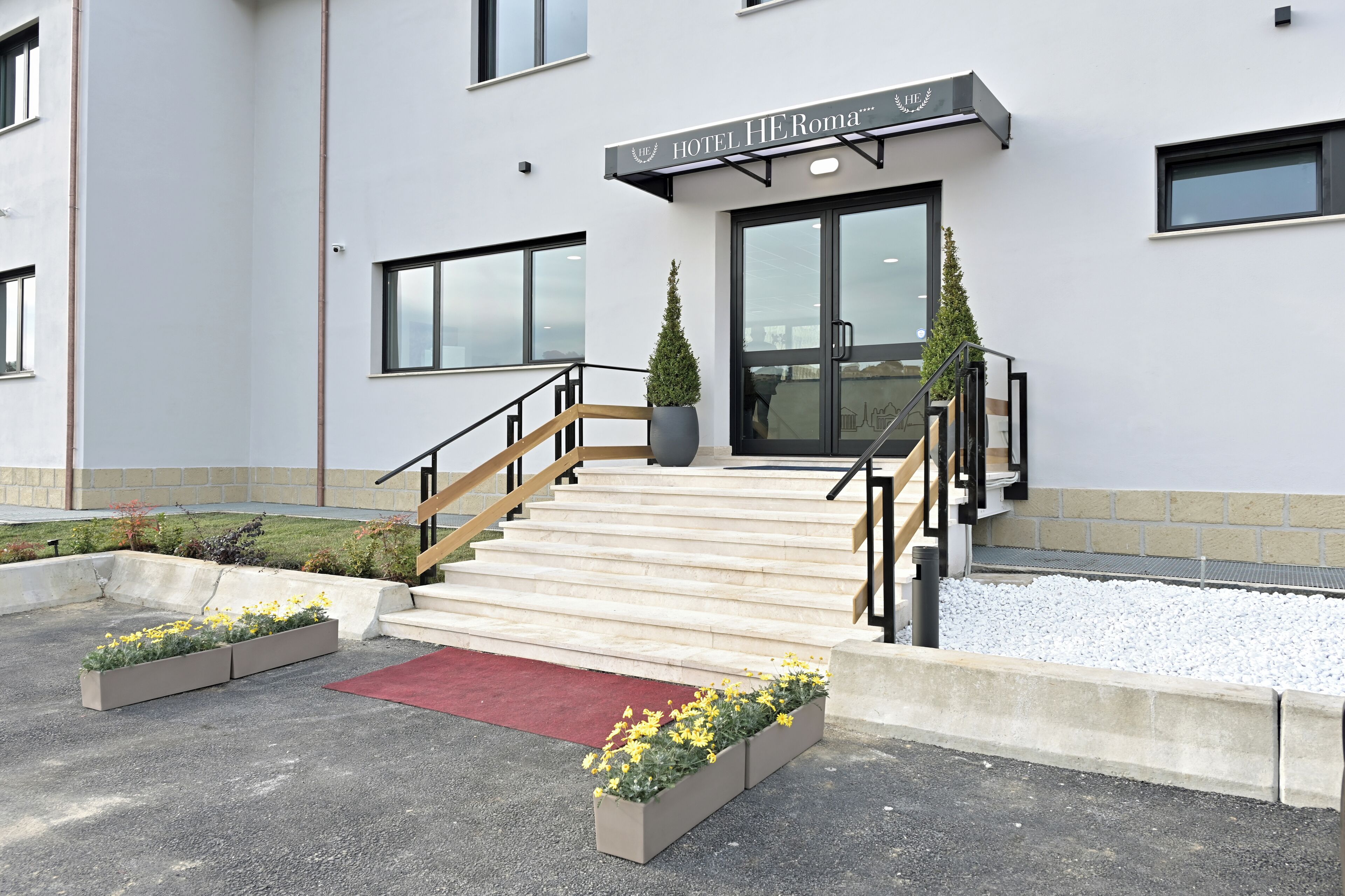 Ein Hotel mit moderner Gestaltung, inklusive einer Treppe zum Eingang, einem roten Teppich und floralen Pflanzgefäßen.