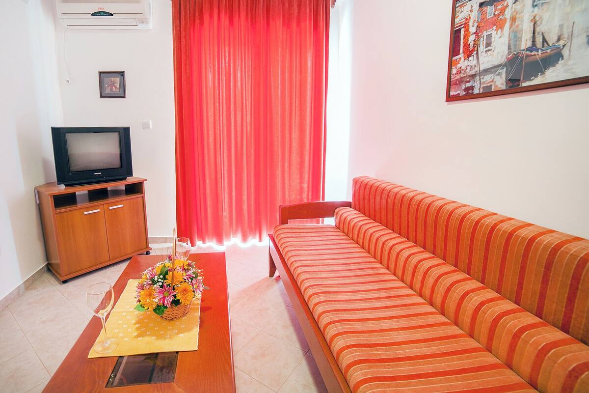 A living room with a sofa, a TV on a wooden stand, a red curtain, and a painting on the wall.
