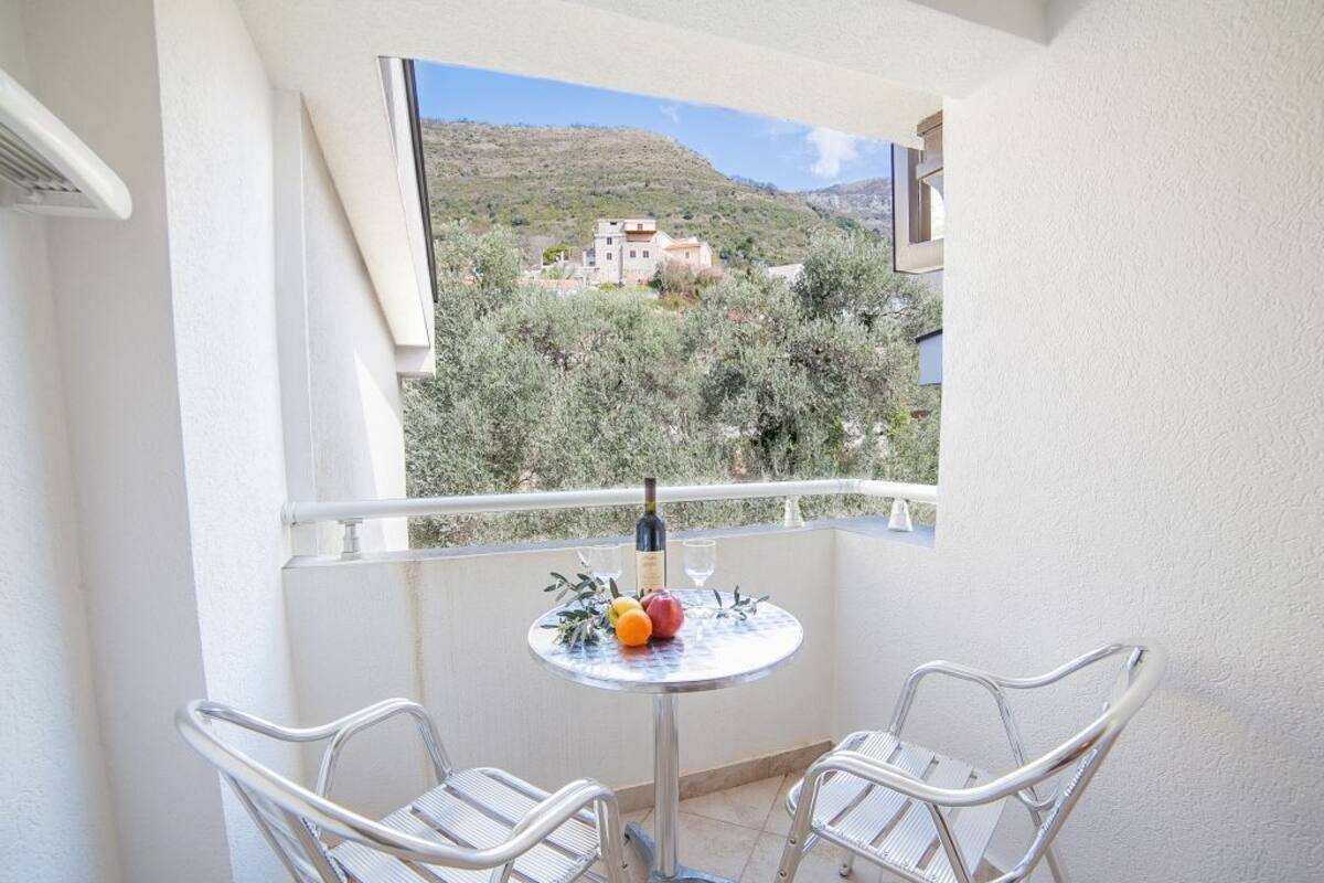 A balcony with two metal chairs, a small round table with a bottle of wine, glasses, and fruit.