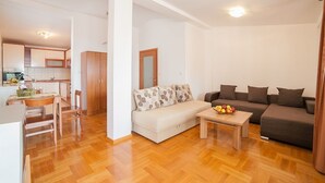 A modern living room with a sofa, a coffee table with fruit, and a dining area with a table and chairs. - Ivan Apartmani (Petrovac)