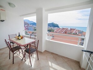 Ein Balkon mit Tisch und Stühlen, Blick auf das Meer und Gebäude, sowie ein gefliester Boden.