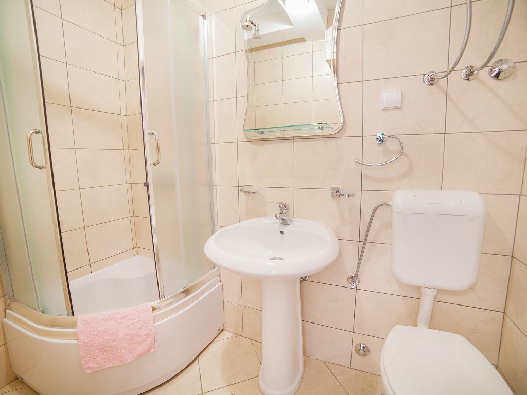 A bathroom with a shower, sink, toilet, and a mirror.
