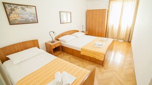 A hotel room with two beds, a wooden wardrobe, a nightstand, and a painting on the wall. - Ivan Apartmani (Petrovac)