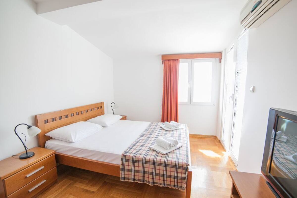 A bedroom with a wooden bed, a nightstand, a TV, and a window with curtains.