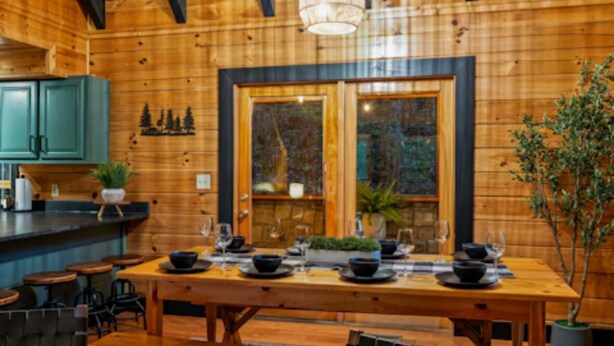 Un intérieur en bois comprenant une table à manger pour quatre personnes, un coin bar et une grande fenêtre donnant sur la forêt.