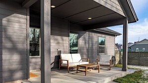 Eine überdachte Veranda mit einer Holzbank und einem weißen Sofa, ein Betonweg und Blick auf eine Wohngegend.