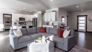 Ein modernes Wohnzimmer mit einem grauen Ecksofa, einem Couchtisch und einer Küche im Hintergrund.