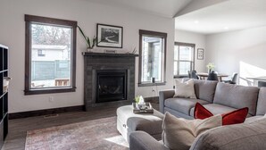 Ein Wohnzimmer mit Kamin, großen Fenstern, einer Couch und einem Essbereich.