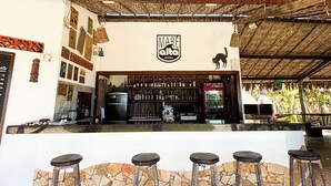An outdoor bar area with a thatched roof, stone flooring, and a bar counter with stools.