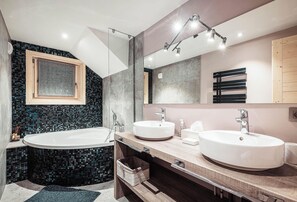 Enjoy a luxurious bathing experience in this bathroom featuring a bathtub, two sinks, and a large mirror.