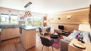 Eine moderne Küche mit Holzausstattung, ein Essbereich mit Tisch für vier Personen, eine Sitzecke mit Sofa und ein Fernseher in einem Wohnbereich mit Holzvertäfelung.