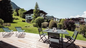 Eine Holzdar Terrasse mit Tisch und Stühlen, mit Blick auf eine grüne Landschaft mit Häusern und Bergen.