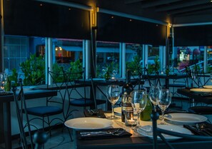 Un restaurante con mesas preparadas para comer, copas de vino y botellas, con vista al exterior.