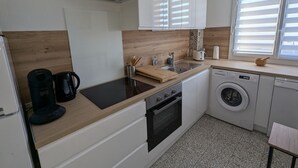 Une cuisine moderne avec des meubles blancs, un plan de travail en bois, un four encastré, un lave-linge et une machine à café.