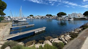 A marina with boats docked, a wooden pier, and buildings in the background. - Sol-y-Days la Santa Maria marinas view (Le Grau-du-Roi)