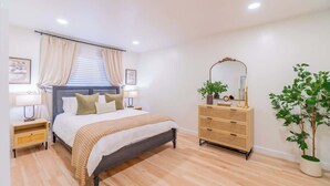 A bedroom with a bed, bedside tables, a dresser, a mirror, and a potted plant. - Emerald Escape - UNR & Pet Friendly - Fenced Yard (Reno)