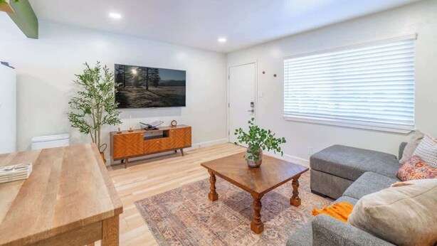 A modern living room with a wooden coffee table, grey sofa, and a flat-screen TV mounted on the wall. - Emerald Escape - UNR & Pet Friendly - Fenced Yard (Reno)