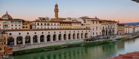 A riverside view of a historic city with a prominent tower and a series of buildings with arched windows and balconies.