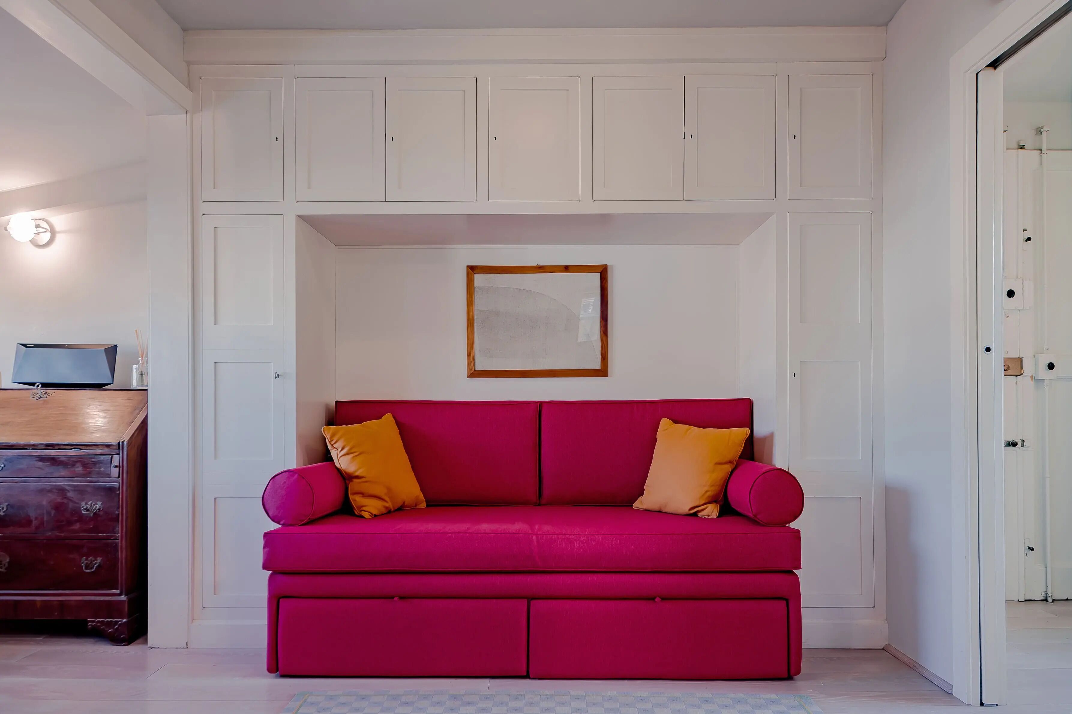 Une pièce avec un canapé rouge, un meuble en bois et des murs blancs.