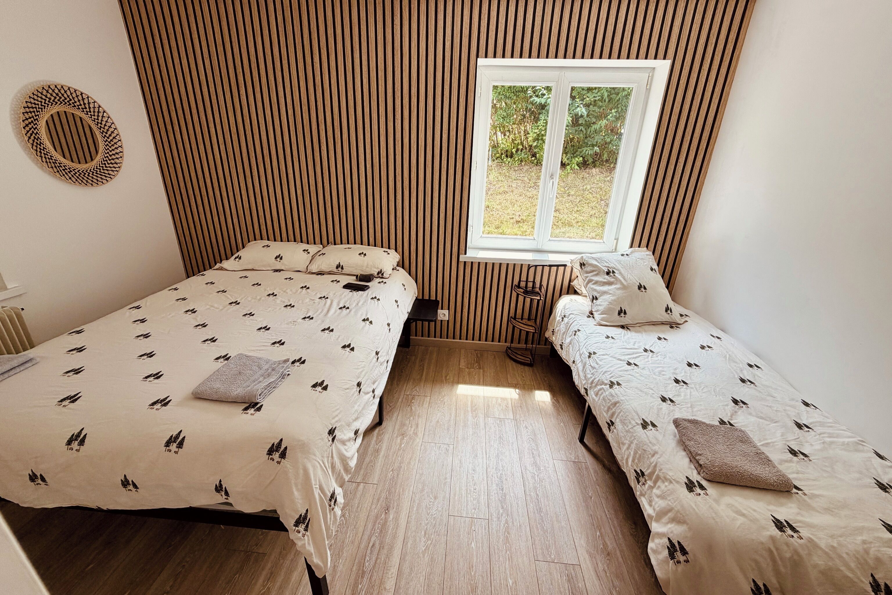 A bedroom with two beds, a window, and a wooden slatted wall.
