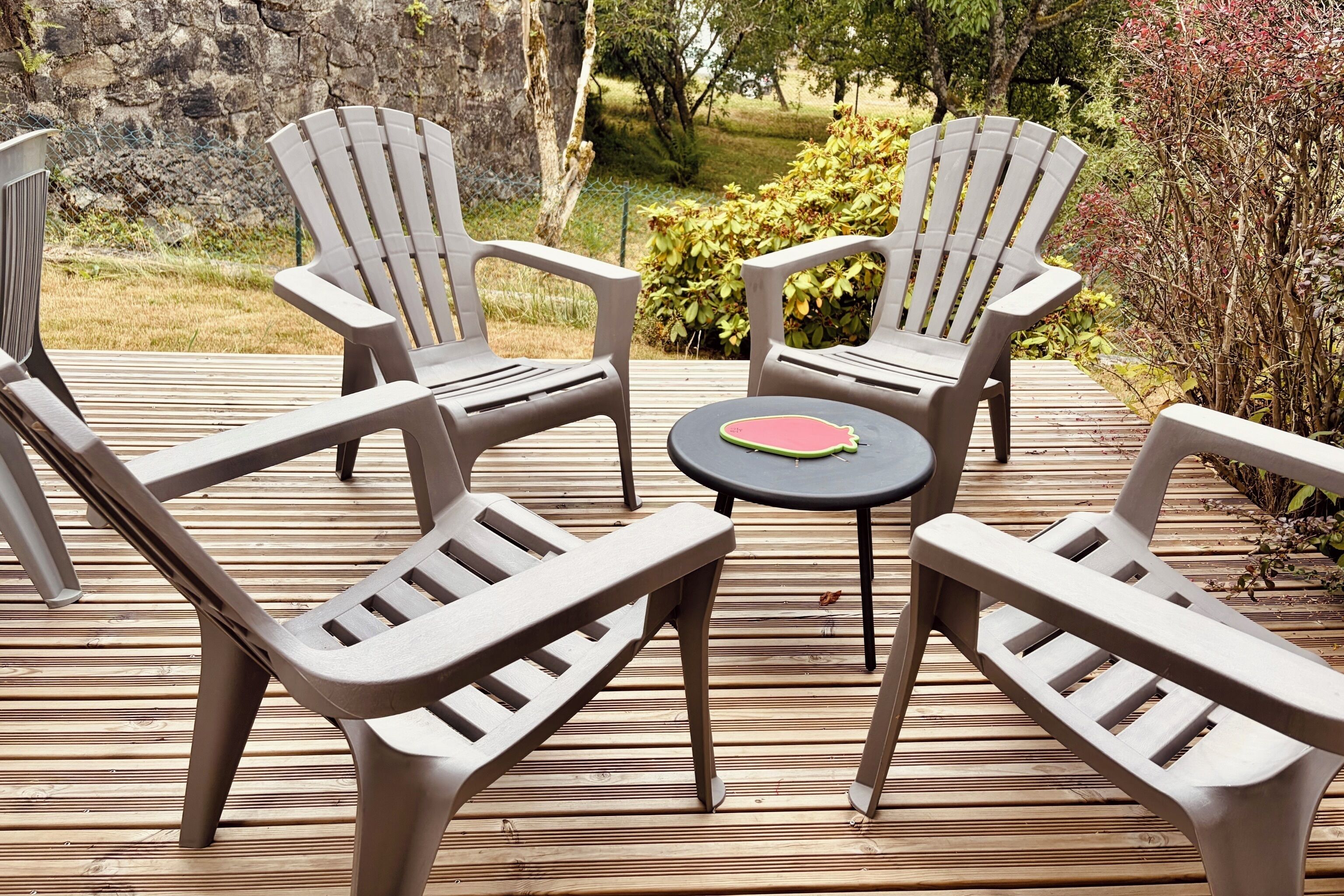 A deck with four Adirondack chairs and a small round table.