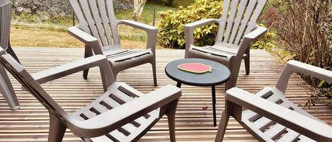 A deck with four Adirondack chairs and a small round table.