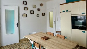 A kitchen with a wooden table, chairs, a refrigerator, and multiple wall clocks.