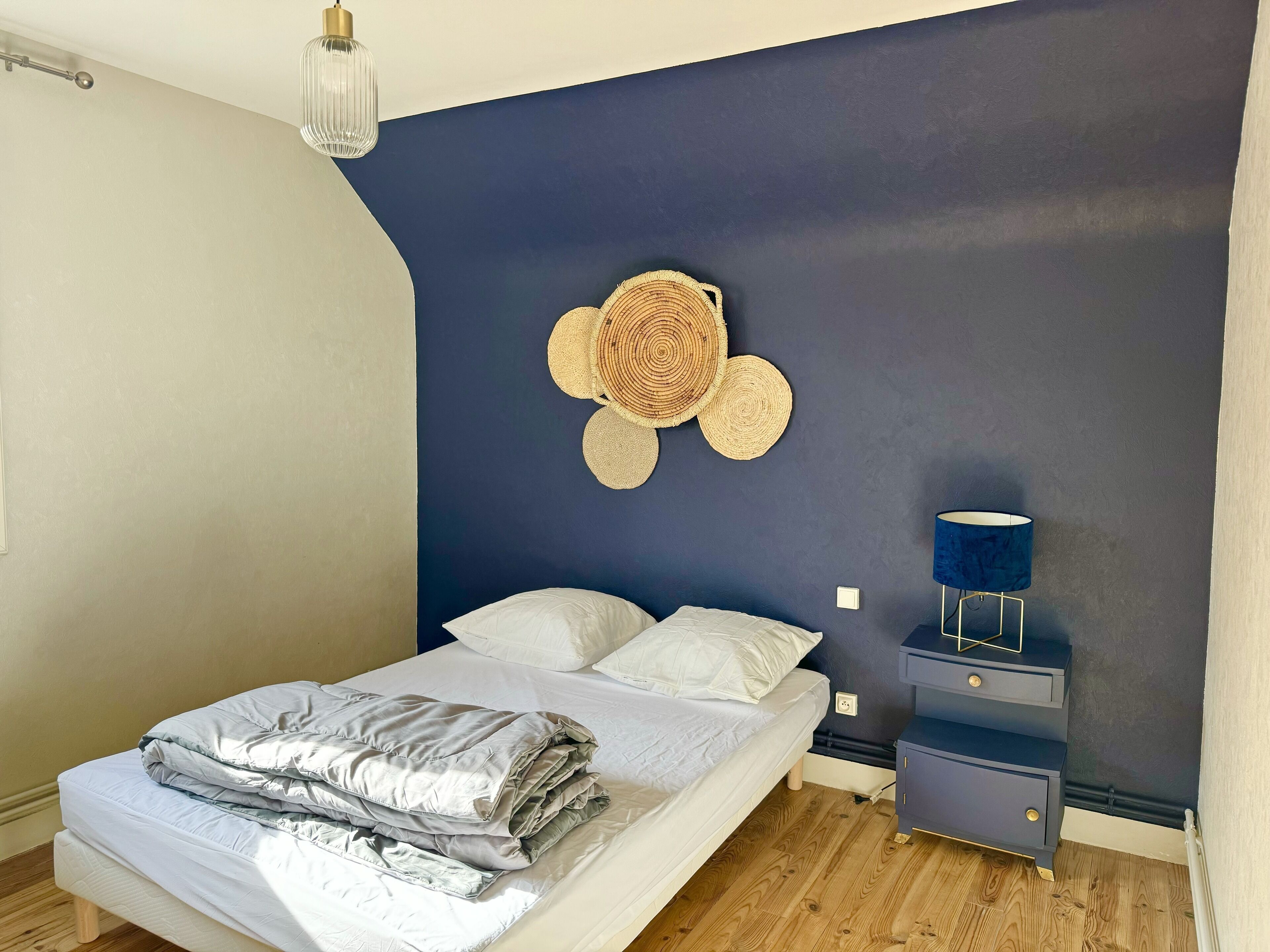 Een slaapkamer met een bed, nachtkastjes, een lamp en een wanddecoratie.