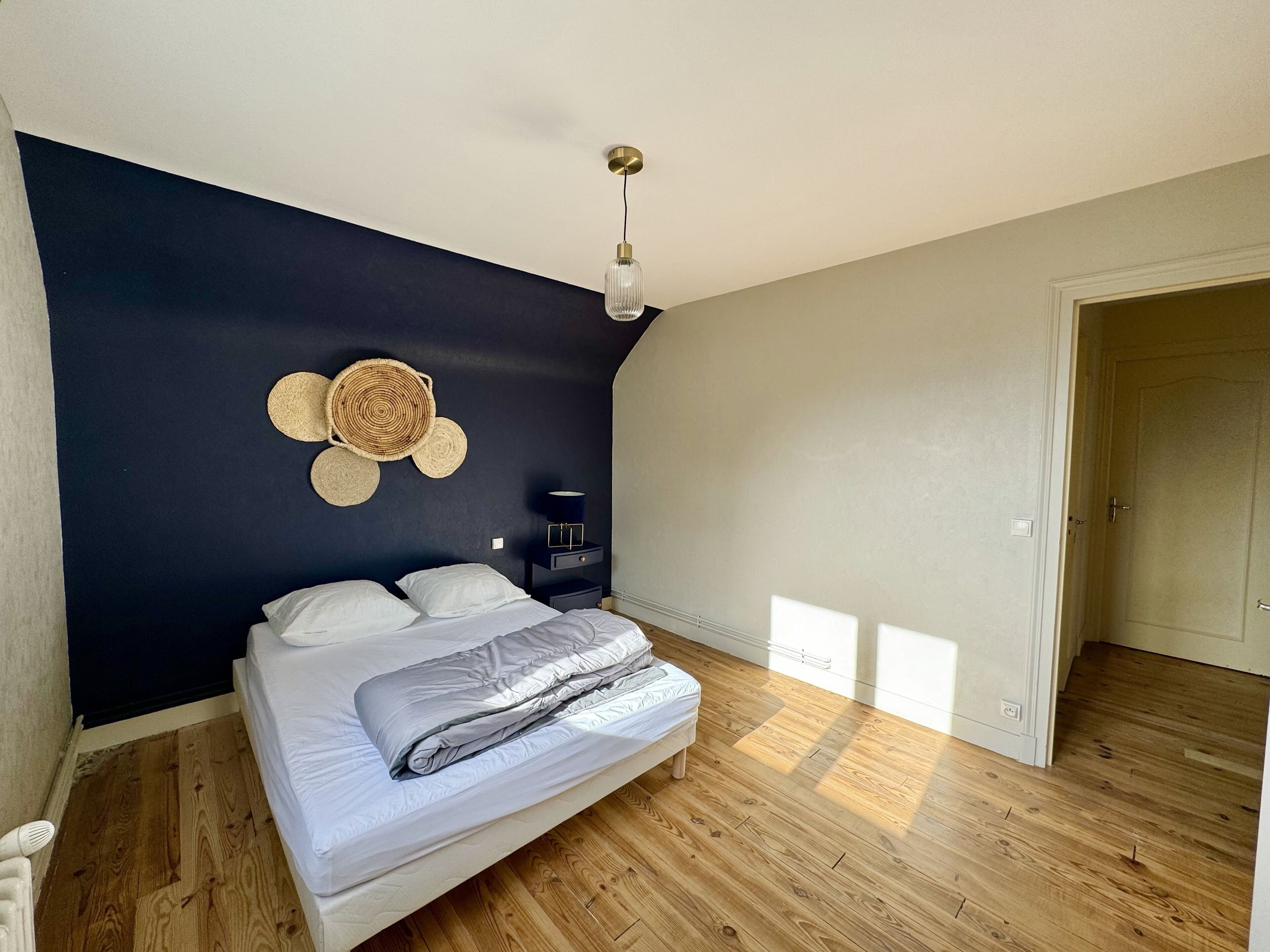 Une chambre à coucher avec un lit, une table de chevet, une lampe fixée au mur et une porte.