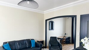 A modern living room with a black leather sofa, a black armchair, a small coffee table, and a dining area in the background.