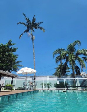 Una piscina con palme, un ombrellone bianco e un'area vetrata.