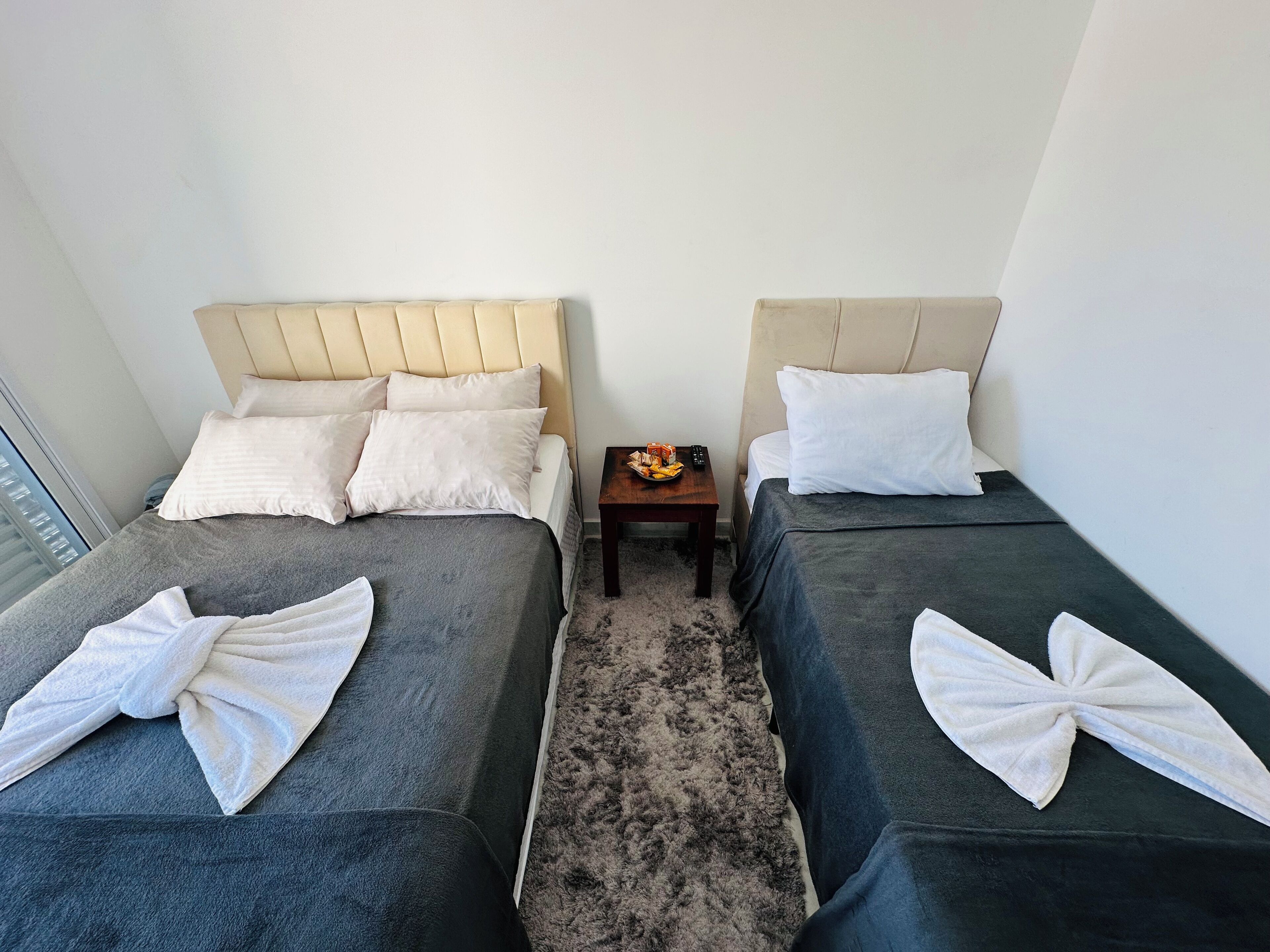 A hotel room with two beds, each with a headboard, a small table with a remote control, and towels on the beds.