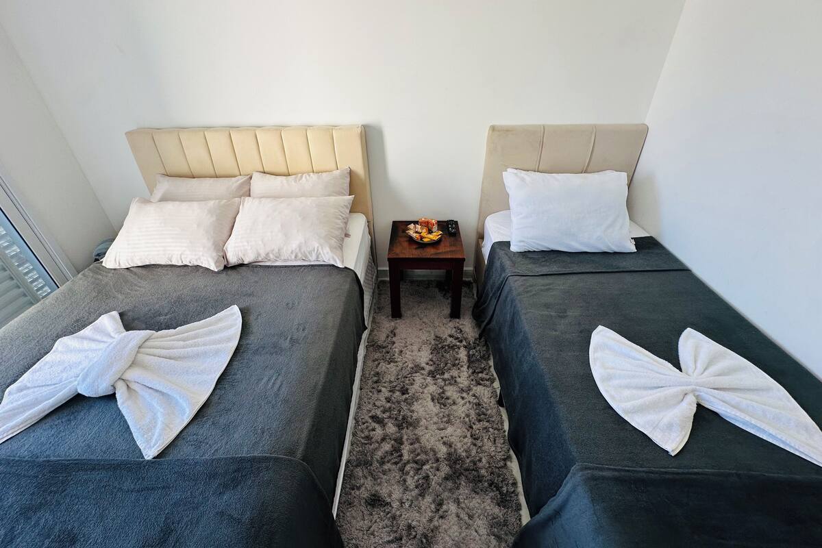 A hotel room with two beds, each with a headboard, a small table with a remote control, and towels on the beds.