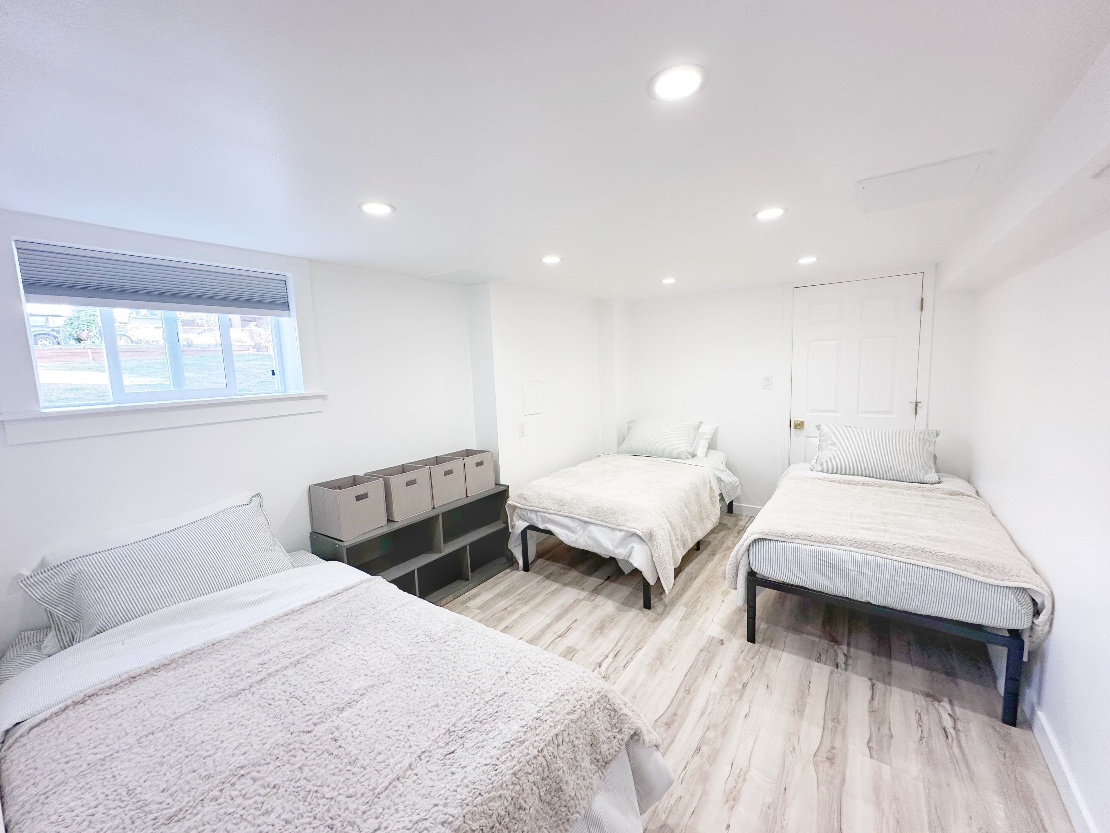 A bedroom with two beds, a window, and storage boxes.