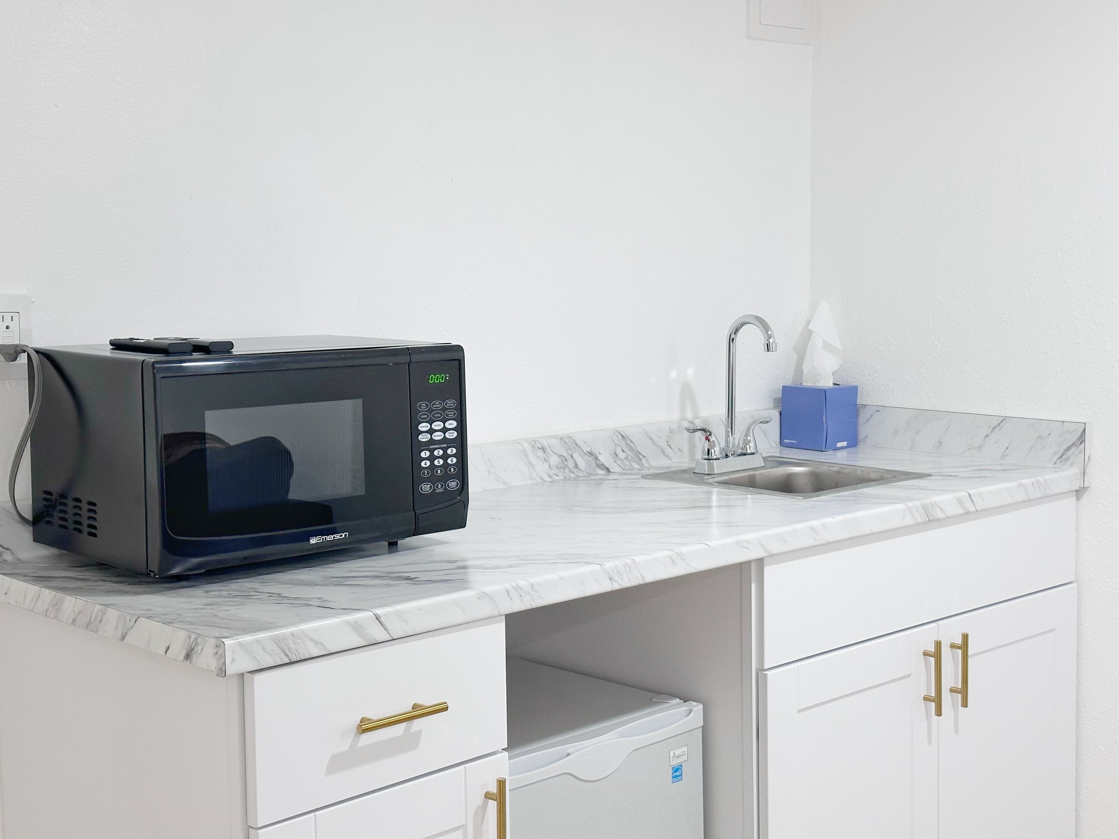 A compact kitchenette with a black microwave, a sink, and a marble countertop.