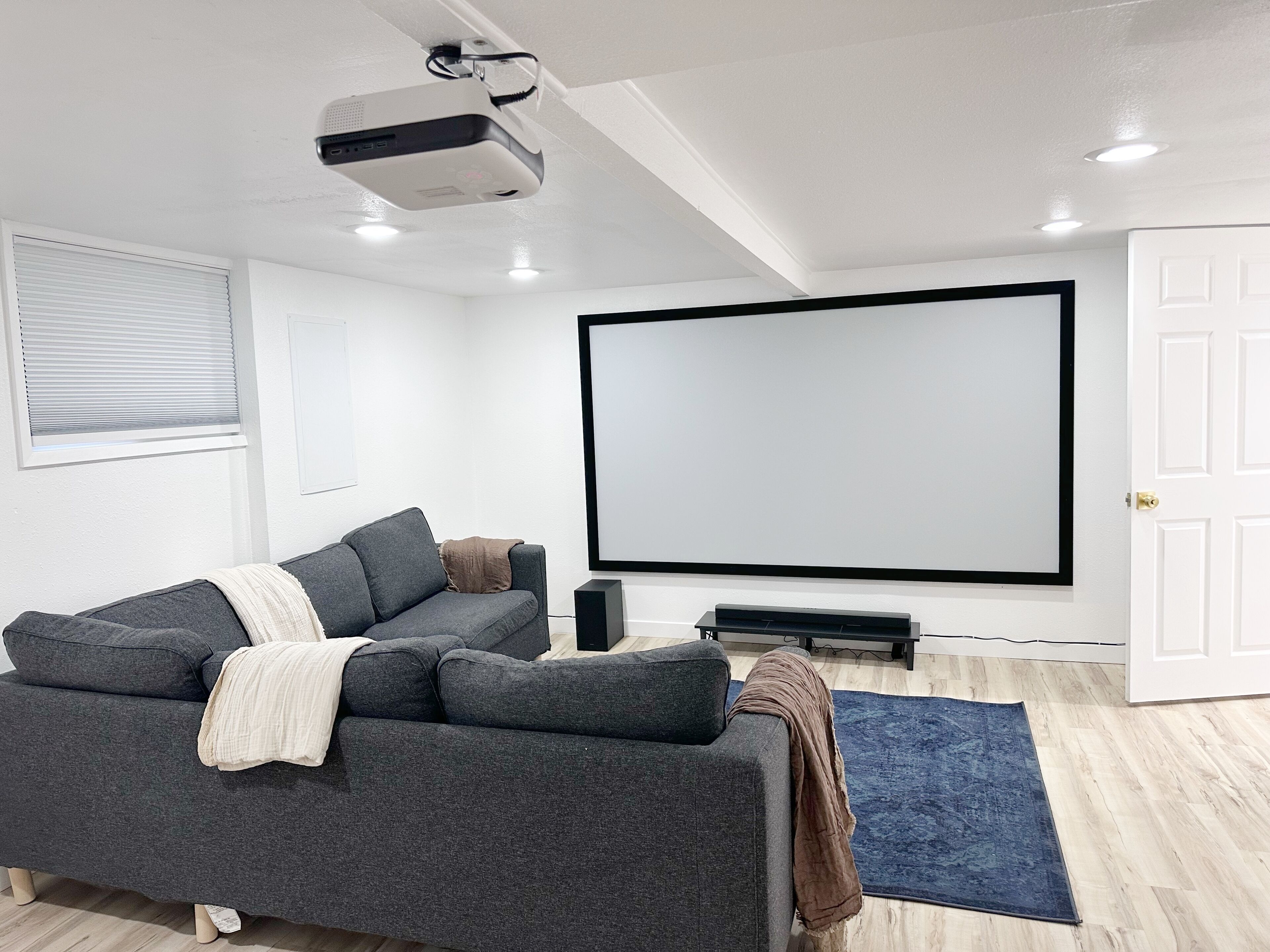 A modern living room with a gray sofa, a large flat-screen TV, and a ceiling projector.