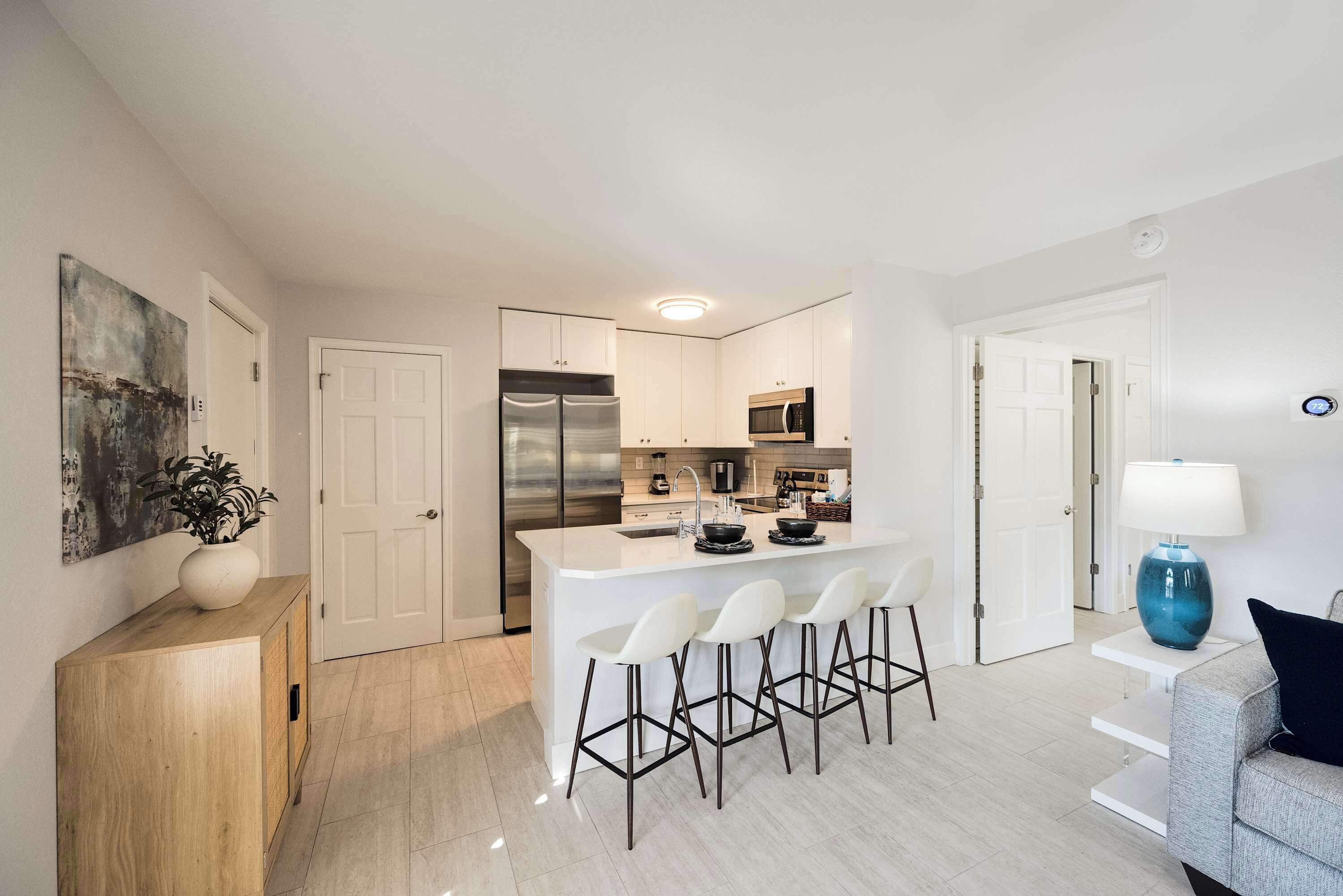 Een moderne keuken met een centraal eiland, witte barstoelen en een zithoek met een grijze bank.