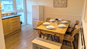 A dining area with a wooden table set for four, a kitchen with wooden cabinets, and a refrigerator. - Theatre Severn Town House, Parking & Quarry Views (Shropshire)